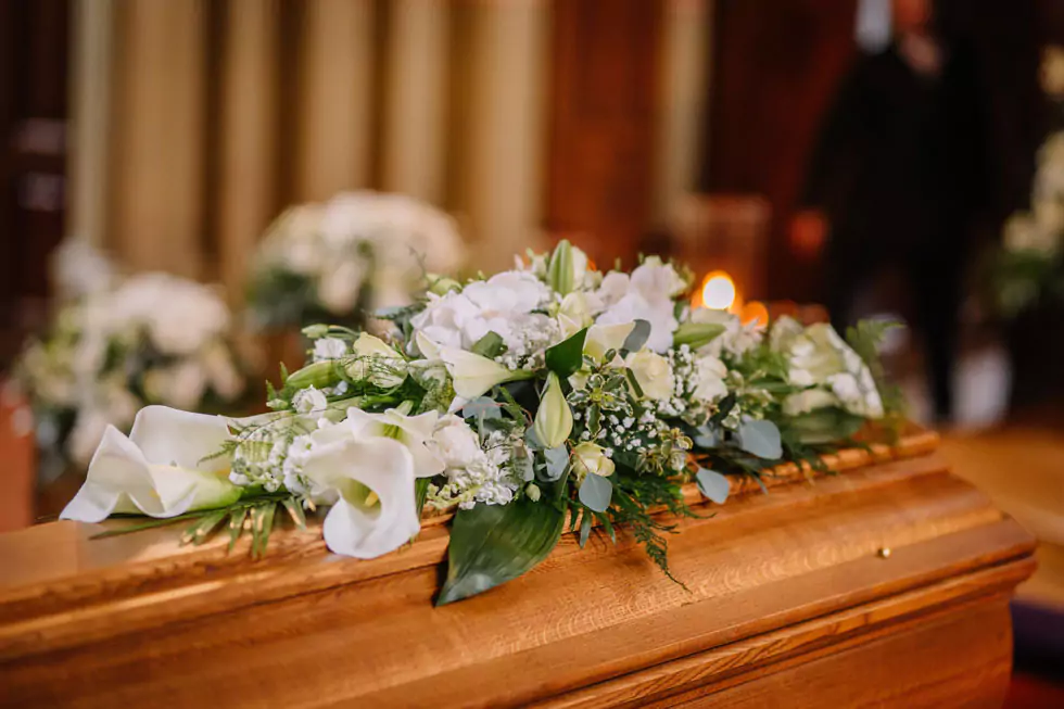 Blumen auf Sarg Nahaufnahme eines Holzsargs, der mit einem Gebinde aus weißen Blumen geschmückt ist