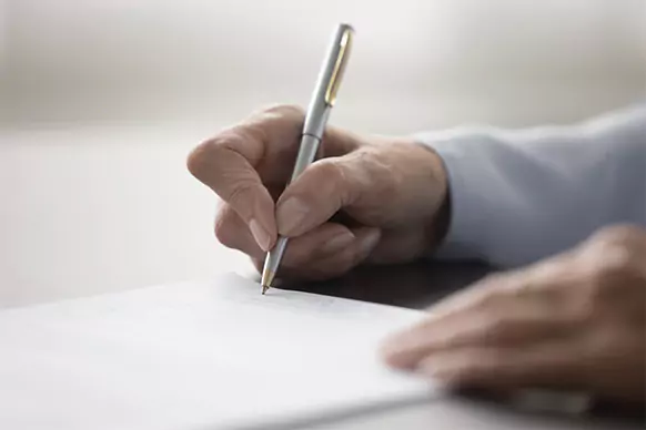 Weibliche Hand, die einen Stift zum Unterschreiben hält Weibliche Hand, die einen Stift zum Unterschreiben hält als Symbolbild für Bestattungsvorsorge